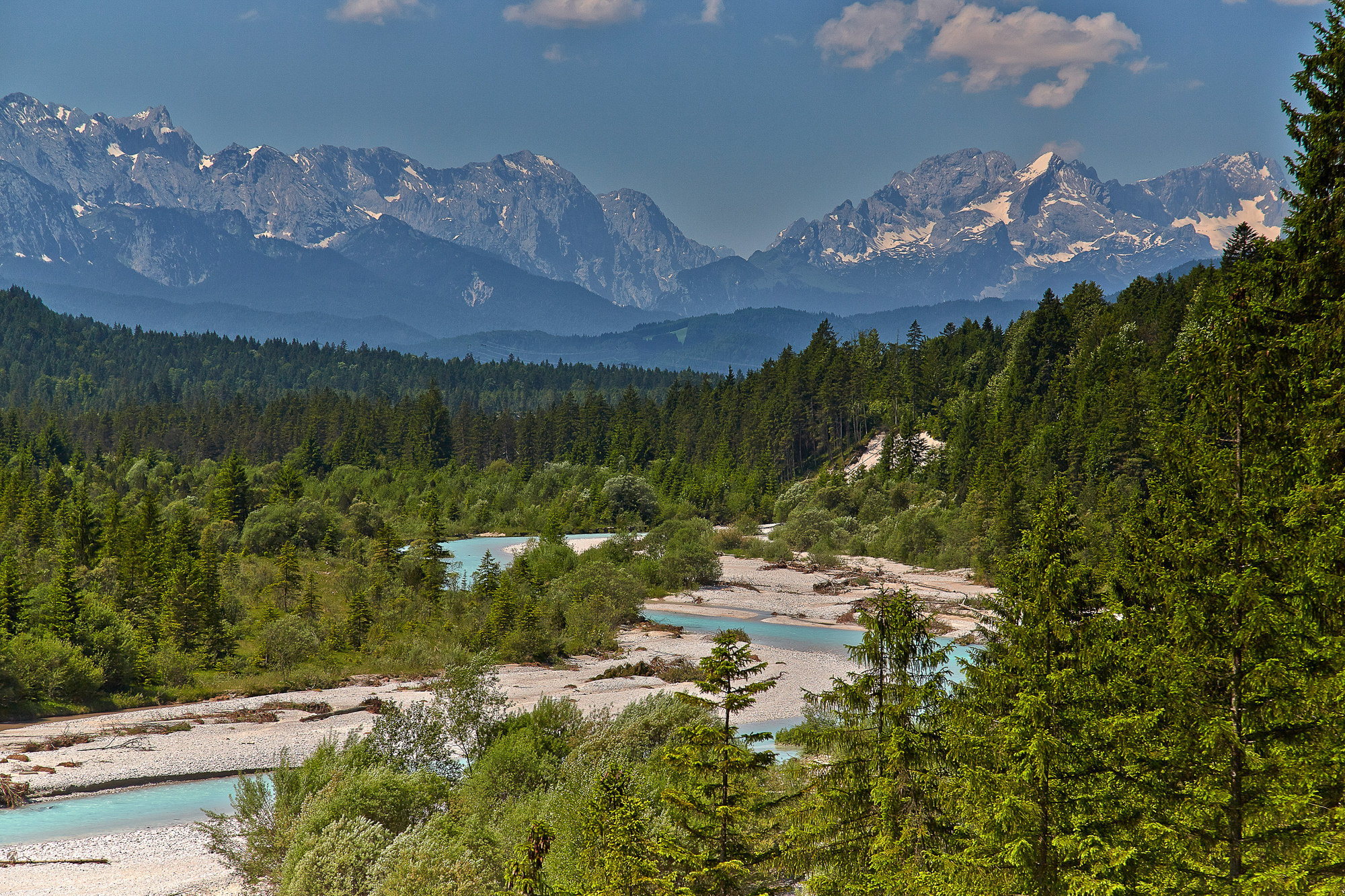The image shows the Isar river valley in Southern Bavaria. The jade colored river is in stark contrast to the rocky mountains in the distance and the green pine trees.